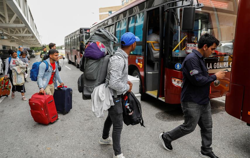 Venezuelan migrants carrying luggage are pictured as they get on a government bus at the Simon Bolivar International airport.