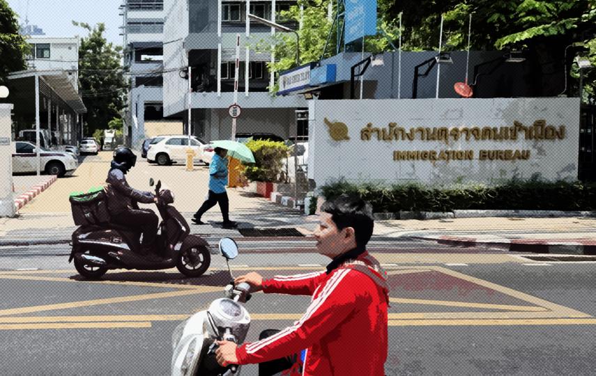 This photo shows the entrance to the Suan Phlu immigration detention centre in Bangkok. We see a person driving a scooter wearing a red jacket in the foreground with the centre in the background. The image is stylized with halftone pattern.