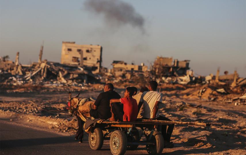 A group of displaced Palestinians are photographed as they travel on a cart with their belongings pulled by a donkey after leaving Rafah in the southern Gaza Strip due to an evacuation order by the Israeli army. In the background you see rubble and smoke.